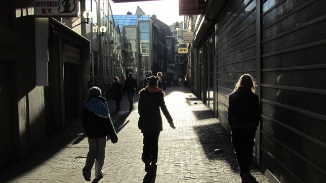 3 kids (~13) walking in an allyway in Amsterdam. The are walking away from the camera an appear to have a edge of light around them,